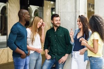 Multi-ethnic group of young people having fun together outdoors in urban background. group of beautiful women and men laughing together. Multi-ethnic group of friends having fun together in urban background