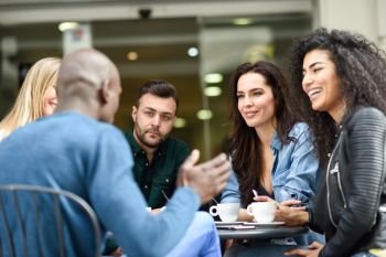 Multiracial group of five friends having a coffee together. Three women and two men at cafe, talking, laughing and enjoying their time. Lifestyle and friendship concepts with real people models. Multiracial group of five friends having a coffee together