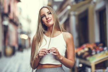 Young woman in urban background. Blond girl wearing with nice hair casual clothes in the street. Straight hairstyle.. Beautiful young blonde woman in urban background.