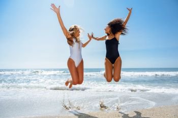 Two funny girls in swimsuit jumping on a tropical beach in summer.. Two funny girls in swimsuit jumping on a tropical beach