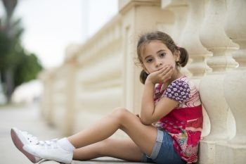 Adorable little girl combed with pigtails outdoors sitting on urban floor.. Adorable little girl combed with pigtails 
