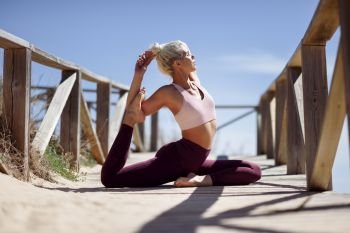 Caucasian woman practicing yoga at seashore. Young female on wooden bridge, Andalusia, Spain.. Caucasian blonde woman practicing yoga in the beach