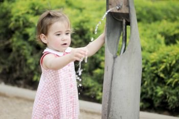 Adorable little girl drinking water in a park fountain. Little girl drinking water in a park fountain