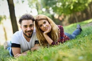 Beautiful young couple laying on grass in an urban park. Caucasian man and woman wearing casual clothes. Blonde female.. Beautiful young couple laying on grass in an urban park. 