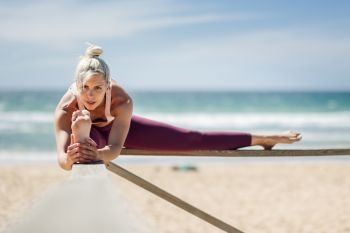 Caucasian woman practicing yoga at seashore. Young female stretching legs in the beach in Cadiz, Andalusia, Spain.. Caucasian blonde woman practicing yoga in the beach