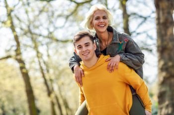Funny couple in a urban park. Boyfriend carrying his girlfriend on piggyback. Love and tenderness, dating, romance. Lifestyle concept. Funny couple in a urban park. Boyfriend carrying his girlfriend on piggyback.