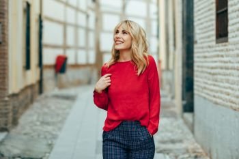 Happy young blond woman walking down the street. Smiling blonde girl with red shirt standing outdoors.. Happy young blond woman walking down the street.