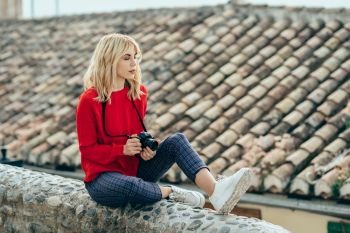Attractive young blond woman enjoying life with eyes closed with an old slr camera in a beautiful city. Blonde happy woman sitting on urban steps.. Attractive young blond woman enjoying life with eyes closed