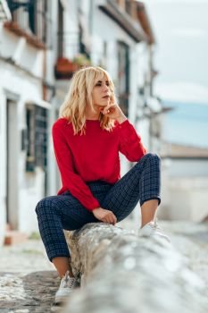 Attractive young blond woman sitting on urban background. Blonde girl with red shirt enjoying life outdoors.. Blonde girl with red shirt enjoying life outdoors.