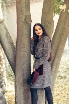 young beautiful girl with very long hair wearing winter coat and cap in urban park full of autumn leaves. Lifestyle and fashion concept.. Girl with very long hair wearing winter coat and cap in urban park full of autumn leaves