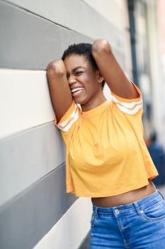 Young African woman laughing near an urban wall. Girl with very short hair wearing casual clothes.. Happy black woman laughing on urban wall.