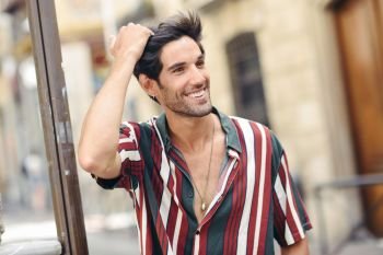 Smiling young man touching his hair wearing casual clothes in urban background.. Smiling young man touching his hair wearing casual clothes outdoors