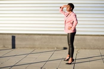 Black woman, model of fashion, standing on urban wall. African american female wearing suit with pink jacket with sunset light.. Black woman, model of fashion, standing on urban wall
