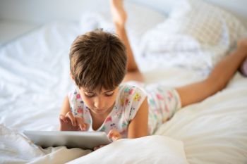 Little girl, eight years old, playing with digital tablet on the bed.. Little girl playing with digital tablet on the bed.