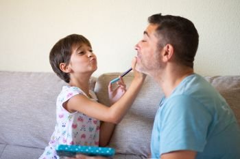 Little cute daughter doing make-up to her father. Dad spending free time with her daughter. Alternative masculinity concept.. Little cute daughter doing make-up to her father