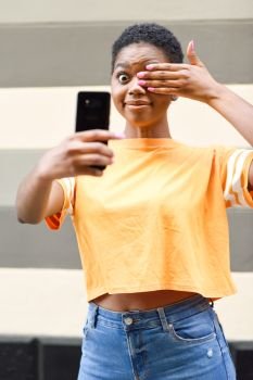 Funny black woman taking selfie photographs with happy expression outdoors. Girl with very short hair wearing casual clothes.. Funny black woman taking selfie photographs with happy expression outdoors