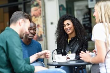 Multiracial group of four friends having a coffee together. Two women and and two men at cafe, talking, laughing and enjoying their time.. Multiracial group of four friends having a coffee together