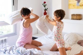 Middle-age mother with her eight years daughter having funny pillow fight on bed. Mum spending free time with her daughter.. Mother and daughter having funny pillow fight on bed.
