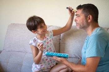 Little cute daughter doing make-up to her father. Dad spending free time with her daughter. Alternative masculinity concept.. Little cute daughter doing make-up to her father
