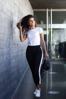Young African woman with black curly hairstyle walking near business building. Happy Arab girl in sport clothes in the street.. Young African woman with black curly hairstyle walking near business building