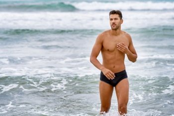 Handsome muscular man bathing on the beach wearing swimwear. Handsome muscular man bathing on the beach