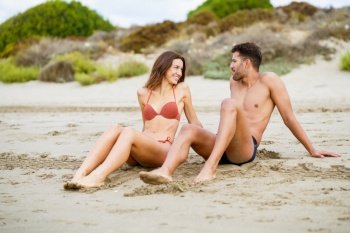 Young couple of beautiful athletic bodies sitting together on the sand of the beach enjoying their holiday at sea. Young couple sitting together on the sand of the beach
