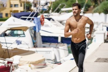 Young man with an athletic body running shirtless through a harbour full of boats.. Young man with an athletic body running shirtless through a harbour.
