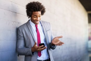 Black Businessman using his smartphone near an office building. Man with afro hair.. Black Businessman using a smartphone near an office building