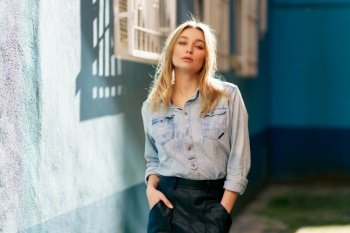 Blonde woman wearing denim shirt and black leather skirt standing in the street. Pretty russian female.. Blonde woman wearing denim shirt and black leather skirt standing in the street.