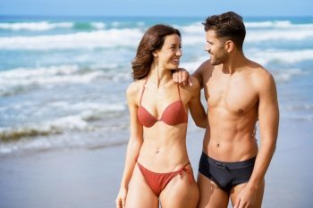Young couple of beautiful athletic bodies walking together on the beach enjoying their holiday at sea. Young couple of beautiful athletic bodies walking together on the beach