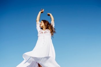 Young beautiful woman raising her arms in a beautiful white dress in Spanish fashion against a blue sky in nature. Young woman raising her arms in a beautiful white dress against a blue sky