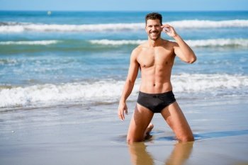 Attractive man on his knees smiling on the sand of the beach. Handsome man on his knees smiling on the sand of the beach