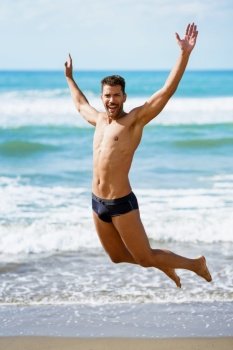 Funny young man with beautiful body in swimwear jumping on a tropical beach.. Young man with beautiful body in swimwear jumping on a tropical beach.