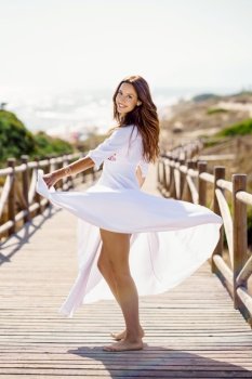 Young pretty woman moving a beautiful white dress in Spanish fashion on a boardwalk on the beach.. Young woman wearing a beautiful white dress in Spanish fashion on a boardwalk on the beach.