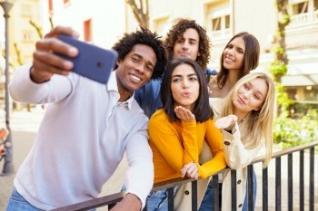 Multi-ethnic group of friends taking a selfie in the street with a smartphone. Young people having fun together.. Multi-ethnic group of friends taking a selfie outdoors with a smartphone.