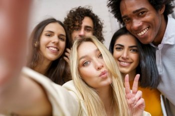 Multi-ethnic group of friends taking a selfie together while having fun in the street. Blonde Russian woman in the foreground.. Multi-ethnic group of friends taking a selfie together while having fun outdoors.