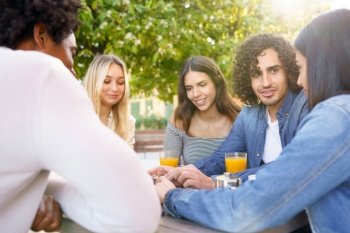 Multi-ethnic group of friends having a drink together in an outdoor bar. One of the men shows something on his smartphone to his friends.. Multi-ethnic group of friends having a drink together in an outdoor bar.