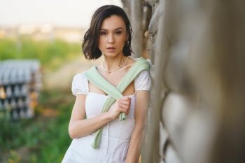 Pretty young Asian woman, posing near a tobacco drying shed, wearing a white dress and green wellies. Beauty and fashion concept. Asian woman, posing near a tobacco drying shed, wearing a white dress and green wellies.