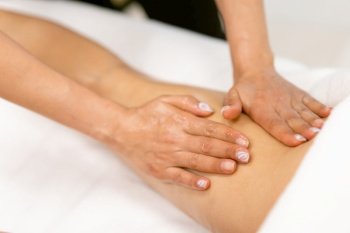 Woman receiving a leg massage with massage candle oil. Body care treatment in a beauty centre.. Beauty salon professional pouring oil from a massage candle on the back of his patient.