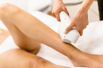 Beautiful woman receiving legs laser hair removal at a beauty center.. Woman receiving legs laser hair removal at a beauty center.