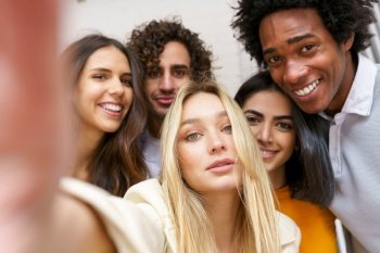 Multi-ethnic group of friends taking a selfie together while having fun in the street. Blonde Russian woman in the foreground.. Multi-ethnic group of friends taking a selfie together while having fun outdoors.