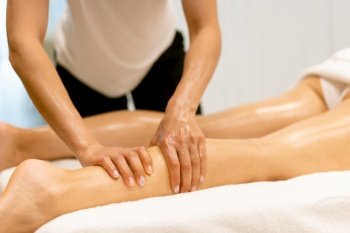 Woman receiving a leg massage with massage candle oil. Body care treatment in a beauty centre.. Beauty salon professional pouring oil from a massage candle on the back of his patient.
