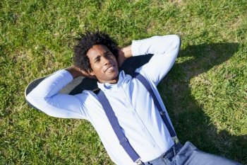 Black businessman with afro hair resting lying on the grass with his skateboard. Black businessman resting lying on the grass with his skateboard