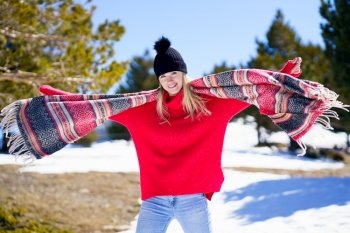 Young happy young blonde woman waving her scarf in the wind in a forest in the snowy mountains in Sierra Nevada, Granada, Andalusia, Spain. Young happy young blonde woman waving her scarf in the wind in a forest in the snowy mountains.