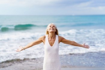 Mature woman opening her arms on a tropical beach, spending her leisure time. Elderly female enjoying her retirement at a seaside retreat.. Mature woman opening her arms on the beach, spending her leisure time, enjoying her free time