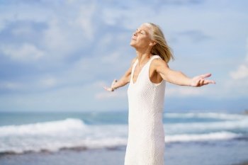 Mature woman breathing the beach air with her eyes closed and her arms open. Elderly female enjoying her retirement at a seaside retreat.. Mature woman breathing the beach air with her eyes closed and her arms open.