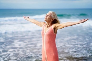 Beautiful mature woman opening her arms on a beautiful beach, spending her leisure time. Elderly female enjoying her retirement at a seaside retreat.. Beautiful mature woman opening her arms on a beautiful beach, enjoying her free time