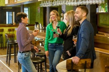 Gleeful diverse man and women with alcohol beverages smiling and talking while spending weekend day in bar together. Happy friends chatting in a beautiful bar