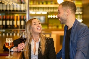 Cheerful multiracial man and woman with alcohol drinks smiling and looking at each other while having date in bar. Happy diverse couple spending time in pub