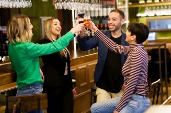 Merry multiethnic adult group of friends in casual clothes smiling and clinking glasses of alcohol drinks while resting near counter in weekend in bar. Happy young people proposing toast in a pub